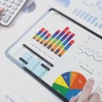 A imagem mostra uma mão usando um tablet com gráficos e dados visuais sobre uma mesa, ao lado de uma calculadora, ideal para análise de métricas de vendas.