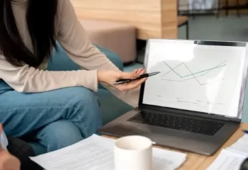 Equipe trabalhando junto em projeto enquanto colega mostra gr&aacute;ficos em notebook