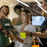 Equipe de profissionais de marketing colaborando e gerenciando estratégias em uma reunião de gestão de equipes de marketing com uso de dispositivos digitais.