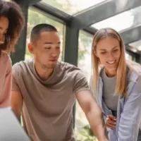 Grupo diverso de pessoas colaborando em um projeto em ambiente moderno, focando na inovação e criatividade. Todos observam um laptop em mesa.