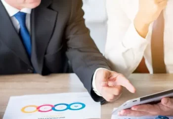 Homem de neg&oacute;cios apontando com o dedo para um tablet digital segurado por seu parceiro no local de trabalho