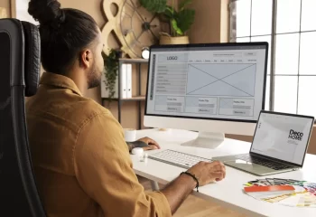 Homem trabalhando em um ambiente de escrit&oacute;rio moderno, avaliando designs em telas, ideal para decora&ccedil;&atilde;o e design de interiores.