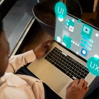 Imagem de uma pessoa utilizando um laptop com elementos gráficos representando design responsivo, UI e UX.