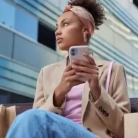 Mulher estilosa com um smartphone, sentada em um banco, cercada por sacolas de compras em ambiente urbano moderno.