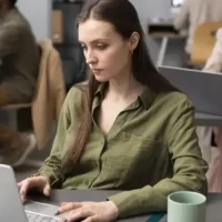 Mulher concentrada trabalhando em laptop em um ambiente de escritório moderno.