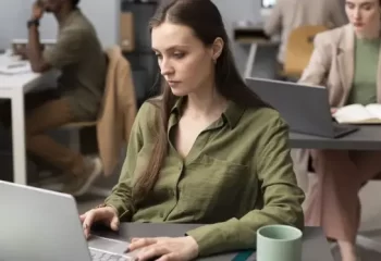 Mulher concentrada trabalhando em laptop em um ambiente de escrit&oacute;rio moderno.