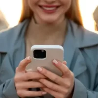 Mulher sorridente usando um smartphone em ambiente urbano ao entardecer, destacando a conexão e a interação moderna.
