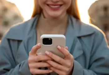 Mulher sorridente usando um smartphone em ambiente urbano ao entardecer, destacando a conex&atilde;o e a intera&ccedil;&atilde;o moderna.