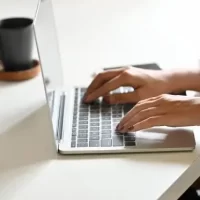 Pessoa digitando em um laptop moderno sobre uma mesa branca.