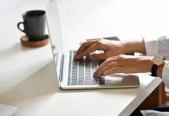 Pessoa digitando em um laptop moderno sobre uma mesa branca.